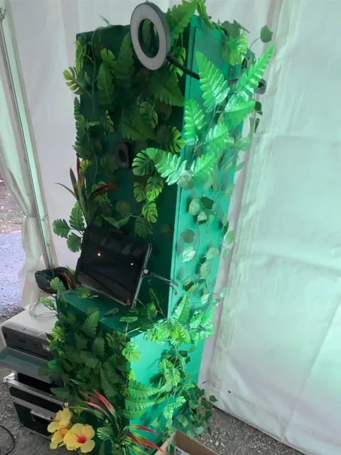 Le Jungleboot installé sous un barnum blanc, décor de fougères et de monstera, imprimante à tirages à sa base